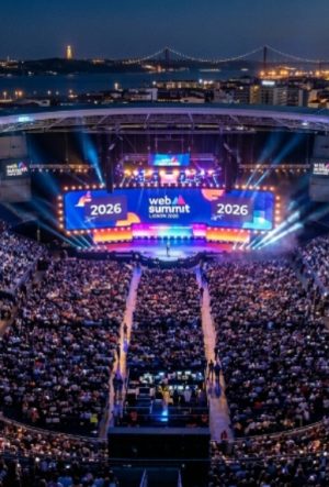Aerial view of a packed Centre Stage audience at Web Summit Lisbon 2026, with bright lights illuminating the Altice Arena during the opening night keynote
