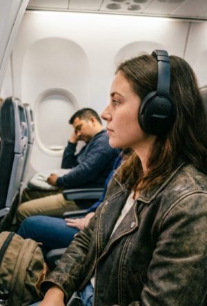 A traveler wearing black Bose QuietComfort headphones while looking out an airplane window.