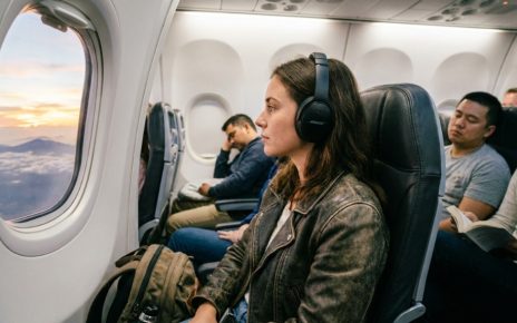 A traveler wearing black Bose QuietComfort headphones while looking out an airplane window.