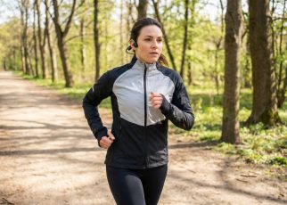 A woman running outside wearing black bone conduction headphones wrapped securely around her ears.