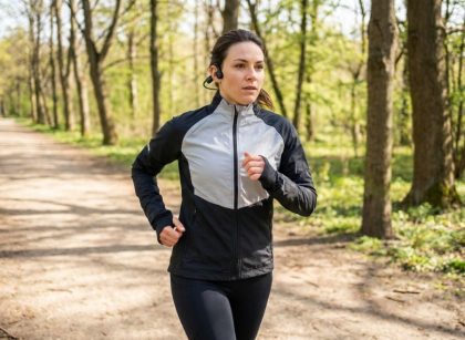 A woman running outside wearing black bone conduction headphones wrapped securely around her ears.