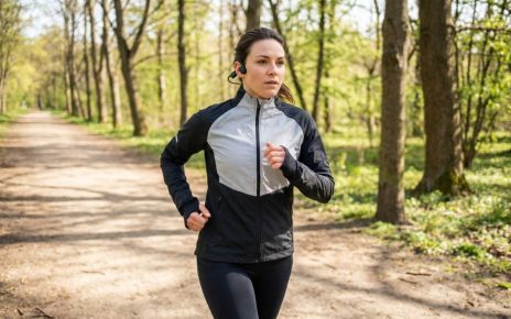 A woman running outside wearing black bone conduction headphones wrapped securely around her ears.